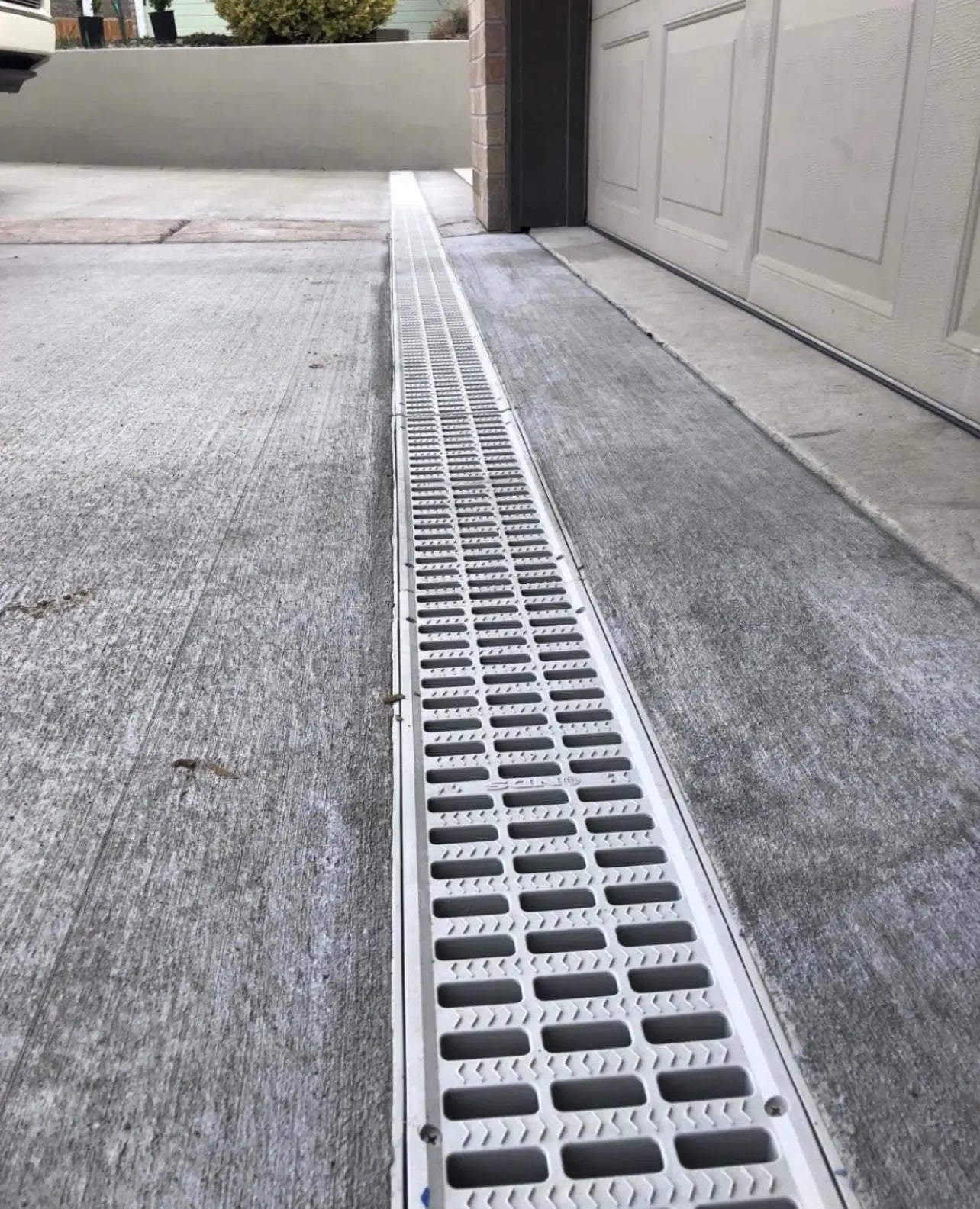 Drainage grate on a driveway next to a garage